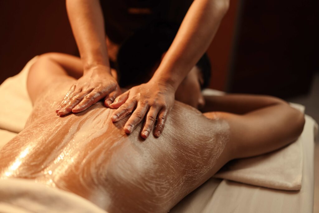 Masseuse appliquant avec les mains un gommage sur le dos de sa patiente pour prendre soin de la peau